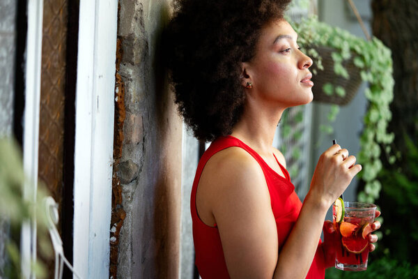 Lifestyle fashion portrait of black woman posing on the street with drink