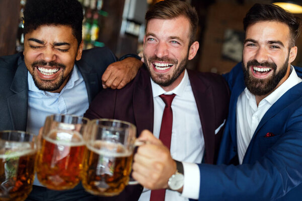 Handsome young businessmen drinking beer, talking and smiling while resting at the pub