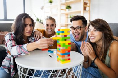 Bir grup genç arkadaş ahşap masa oyunu oynarken eğleniyor. Çok ırklı, neşeli insanlar birlikte eğleniyor ve gülümsüyor.