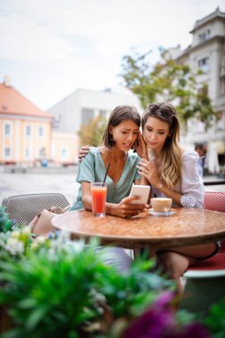 Gerçek arkadaşlar her zaman yakınlardadır. Arkadaşı tarafından teselli edilirken cep telefonu tutan depresyondaki genç bir kadın.