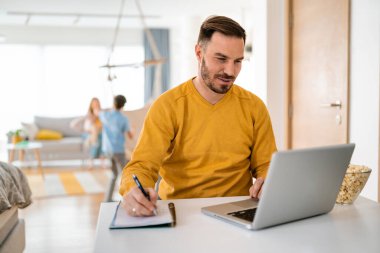 Evde dizüstü bilgisayarla çalışan yakışıklı bir adam.