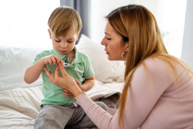Anne hasta çocuğunun sıcaklığını kontrol ediyor.