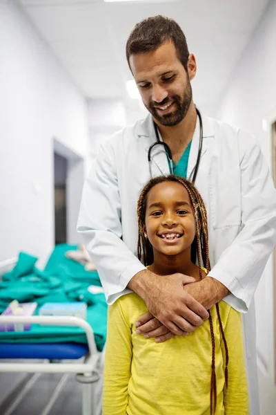 ハンサムな小児科医先生笑顔とともに彼の女の子患者に病院 — ストック写真