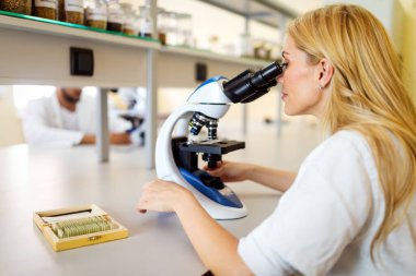 Laboratuvarda mikroskop kullanan bir kadın koronavirüs için test yapıyor.