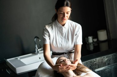 Masör spa salonunda genç kadın vücuduna masaj yapıyor.