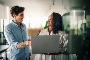 İki farklı etnik çeşitlilikte mutlu iş adamı şirket ofisinde dizüstü bilgisayar kullanarak konuşuyorlar. İş yerindeki meşgul iş adamları ve kadın meslektaşları.
