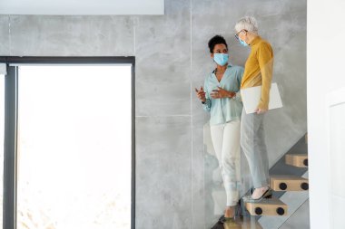 Modern ofiste maske takan iş kadınları, laptopla takım çalışması, salgın sırasında profesyonel iletişim ve işyeri güvenliği