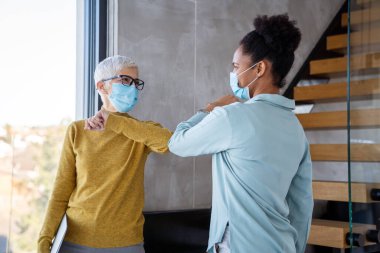 Modern ofiste maske takan iş kadınları, laptopla takım çalışması, salgın sırasında profesyonel iletişim ve işyeri güvenliği