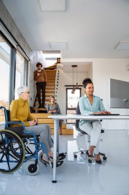 Farklı profesyonellerden oluşan bir grubun birlikte çalıştığı parlak, çağdaş bir ofis. Tekerlekli sandalye kullanan birini de kapsar.