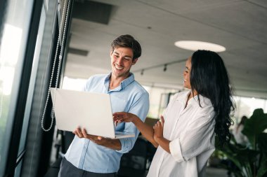 İki farklı etnik çeşitlilikte mutlu iş adamı şirket ofisinde dizüstü bilgisayar kullanarak konuşuyorlar. İş yerindeki meşgul iş adamları ve kadın meslektaşları.