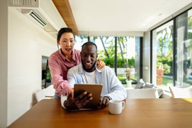 Evde dizüstü bilgisayarlı, yatırım, tasarruf ve faturalar için bütçe planlayan çok ırklı mutlu çift. Çevrimiçi bankacılık ve çeşitli, çok ırklı karı ve kocalarla finansal ödeme
