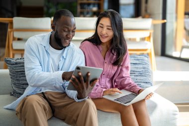 Evde dizüstü bilgisayarlı, yatırım, tasarruf ve faturalar için bütçe planlayan çok ırklı mutlu çift. Çevrimiçi bankacılık ve çeşitli, çok ırklı karı ve kocalarla finansal ödeme