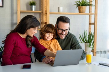Çocuklu mutlu bir aile birlikte dizüstü bilgisayar kullanarak eğleniyor, ebeveynler ve çocuklar evde gülüyor bilgisayarla komik bir internet videosu izliyor, online arama yapıyor.