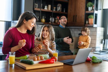 Mutlu ebeveynler mutfak tezgahında çocuklarıyla yemek tarifi hakkında konuşuyorlar ve birlikte hafta sonunun tadını çıkarıyorlar.
