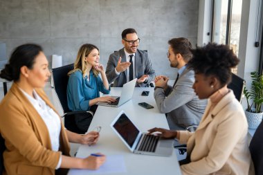 Ofiste yeni bir proje üzerinde çalışırken gülen iş adamları. Modern bir çalışma alanında çalışırken bilgisayar kullanan bir grup farklı iş adamı..