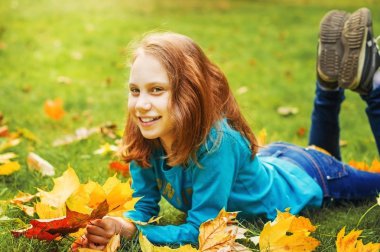 Kız okul çağındaki çocuk Sonbahar Park, yeşil çim üzerinde yalan atar yaprakları.