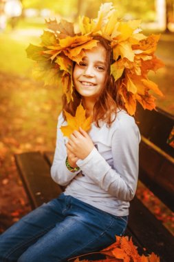 Kız okul çağındaki güzel güneşli Sonbahar Park yaprakların bir çelenk içinde oturuyor.