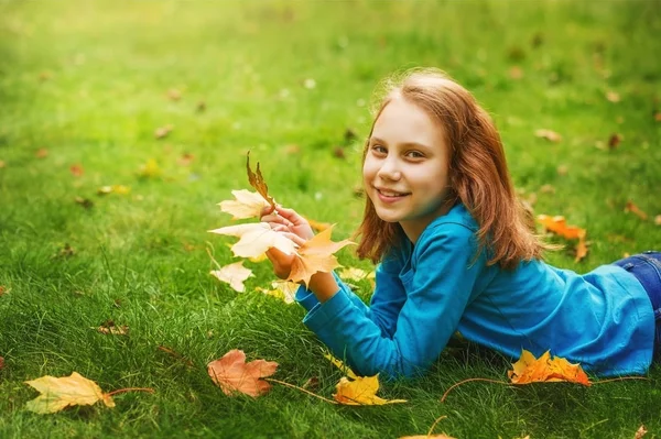 Kız okul çağındaki çocuk Sonbahar Park, yeşil çim üzerinde yalan atar yaprakları.