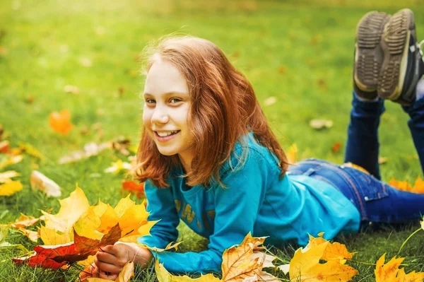 Kız okul çağındaki çocuk Sonbahar Park, yeşil çim üzerinde yalan atar yaprakları.