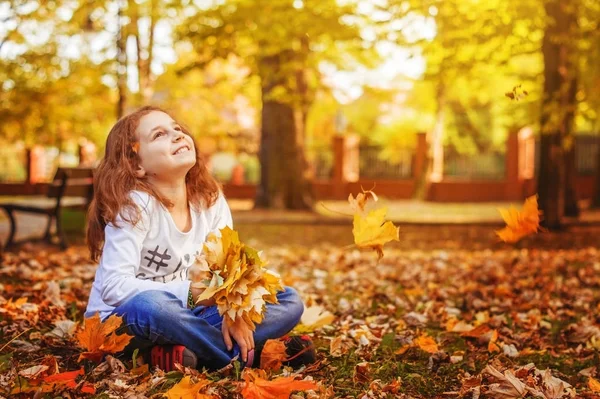 Kız çocuk onun elinde yaprakları ile Sonbahar Park çimlerde oturuyor hayal.