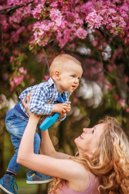 Bir çiçek bahçesinde yürüyüşe kucağında bir bebekle sarışın kadın anne, güzel kız.