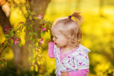 Küçük şirin ve neşeli bebek kız, sarışın kız, güneşli bir bahçede yürüyüş.