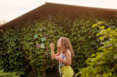 Kabarcıklar yaz bahçede günbatımında üfleme kız çocuk.