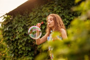 Kabarcıklar yaz bahçede günbatımında üfleme kız çocuk.