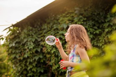 Kabarcıklar yaz bahçede günbatımında üfleme kız çocuk.