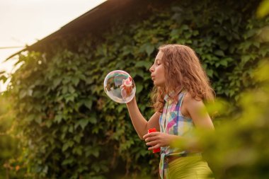 Kabarcıklar yaz bahçede günbatımında üfleme kız çocuk.