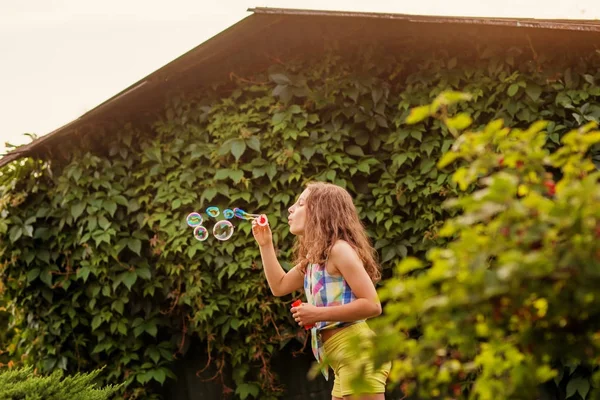 Kabarcıklar yaz bahçede günbatımında üfleme kız çocuk.