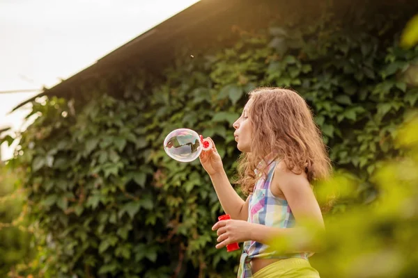 Kabarcıklar yaz bahçede günbatımında üfleme kız çocuk.