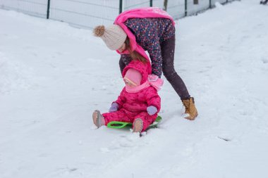 Küçük kız kardeş ile kız şehirde karda kışın binmek.