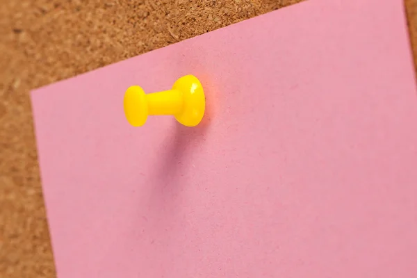 Pink paper pined with yellow tack on brown cork board background.