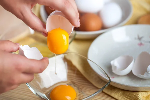 Woman hands breaking an egg to separate egg white and yolks, egg shells at the background.