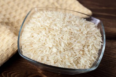 Ahşap masa üzerinde cam kase, yemek pişirmek için madde beyaz pirinç tohumları.