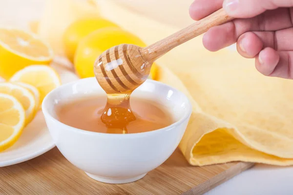 honey in a white ceramic bowl with honey dipper and lemon on a wooden kitchen board.