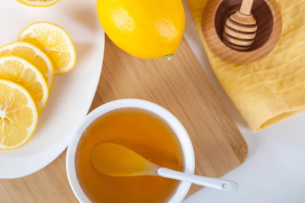 蜂蜜在一个白色的陶瓷碗与勺子和柠檬在木制的厨房板 — 图库照片