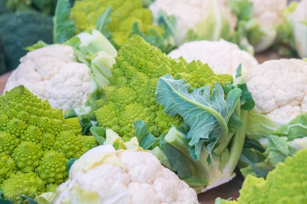 fresh cauliflower with white heads and green leaves at weekly market.