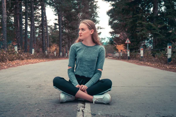 Boş bir yolun ortasında oturan güzel sarışın kız