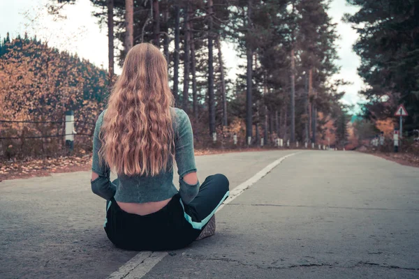 Boş bir yolun ortasında oturan güzel sarışın kız