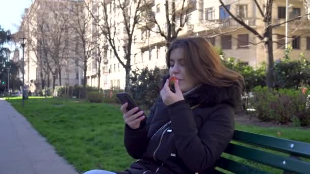 Ελκυστικό Κορίτσι Μιλάει Στο Τηλέφωνο Και Τρώγοντας Φράουλες Στο Πάρκο — Αρχείο Βίντεο