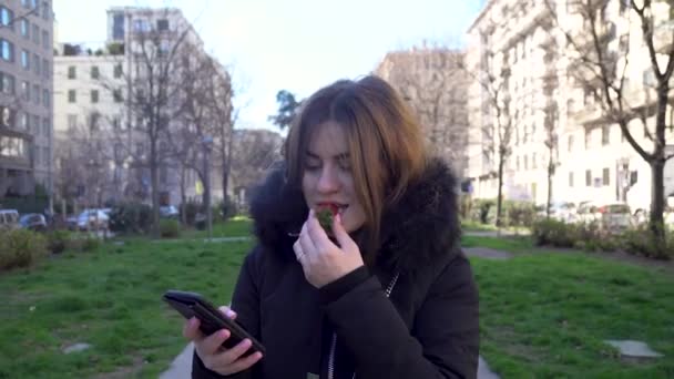 Ελκυστικό Κορίτσι Μιλάει Στο Τηλέφωνο Και Τρώγοντας Φράουλες Στο Πάρκο — Αρχείο Βίντεο