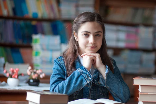 Belle écolière assise dans la bibliothèque et lisant un livre — Photo