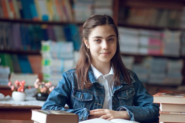 Belle écolière assise dans la bibliothèque et lisant un livre — Photo