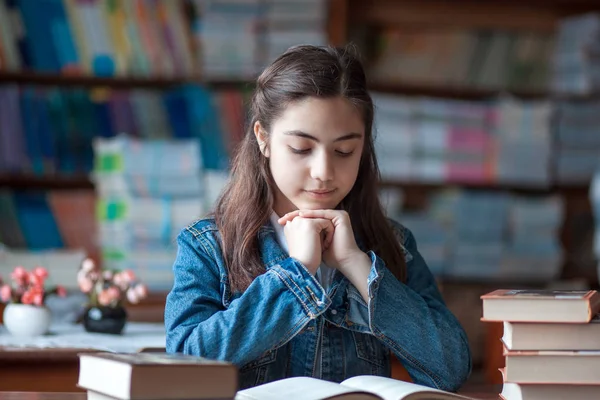 Belle écolière assise dans la bibliothèque et lisant un livre — Photo