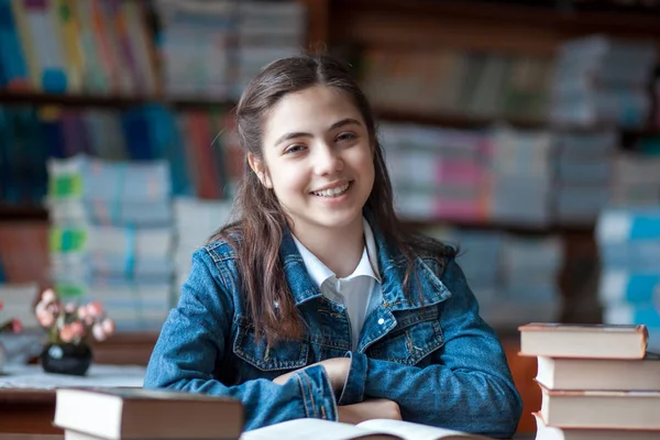 Belle écolière assise dans la bibliothèque et lisant un livre — Photo