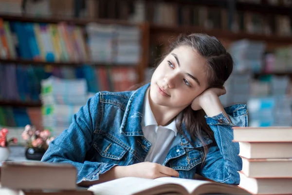 Bela estudante sentada na biblioteca e lendo um livro — Fotografia de Stock