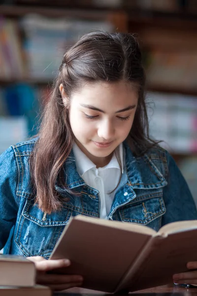 Belle écolière assise dans la bibliothèque et lisant un livre — Photo