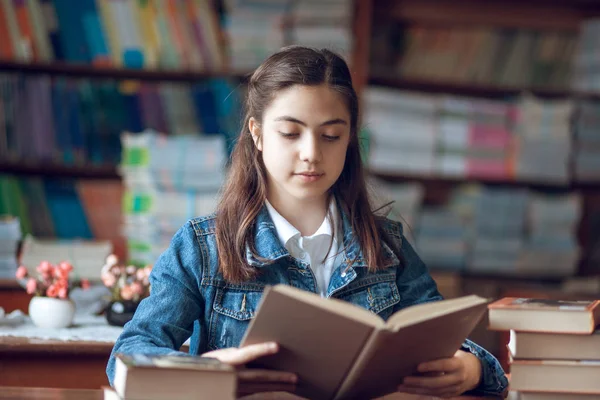 Bela estudante sentada na biblioteca e lendo um livro — Fotografia de Stock